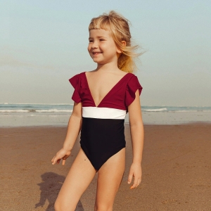 Petite fille blonde souriante à la plage portant un maillot de bain une pièce
