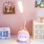 Veilleuse LED en forme de lapin pour fille couleur rose sur une table à coté d'une horloge.