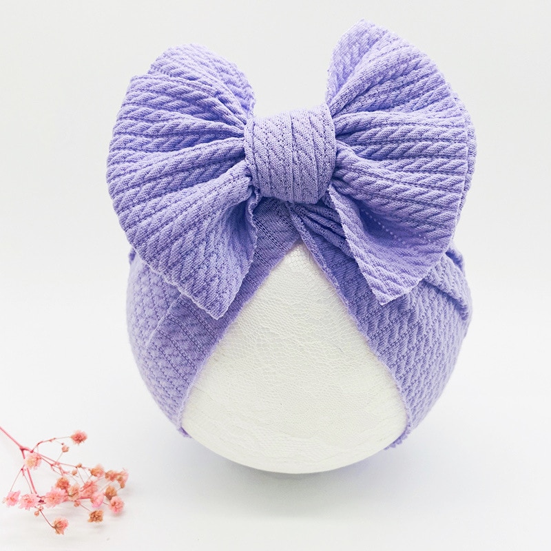 Bandeau à noeud papillon pour bébé fille de couleur violet posé sur une boule blanche à côté de fleurs roses