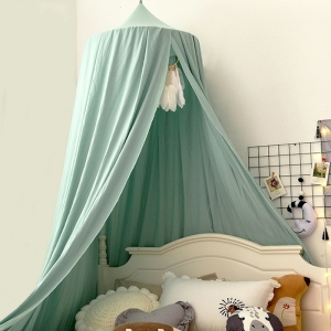 Dessus de berceau pour bébé de couleur verte suspendu au dessus d'un lit blanc avec des oreillers de couleurs blanc, beige, gris devant un mur blanc