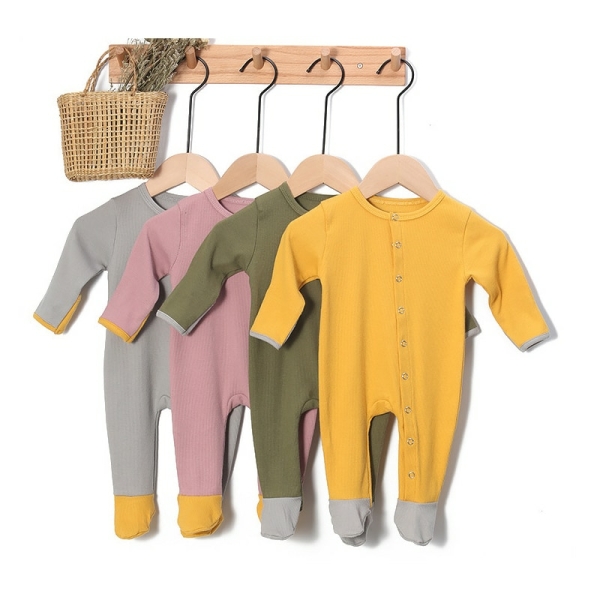Grenouillère côtelée pour bébé en coton de couleur jaune, vert, rose et gris suspendu avec un panier en osier par des cintres sur un porte manteau mural de couleur beige