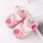Sandale pour fille de couleur rose avec 4 petites fleurs de couleurs différentes, posée sur un magazine et une table blanche
