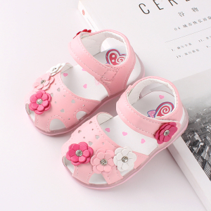 Sandale pour fille de couleur rose avec 4 petites fleurs de couleurs différentes, posée sur un magazine et une table blanche