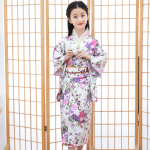 devant un paravent japonais, une fillette porte un kimono traditionnel blanc avec motif fleuri rose