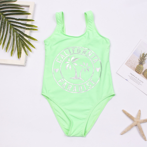 présenté à plat près d'une feuille de palmier, une étoile de mer et un magazine, un maillot de bain vert fluo avec écriture devant argentée