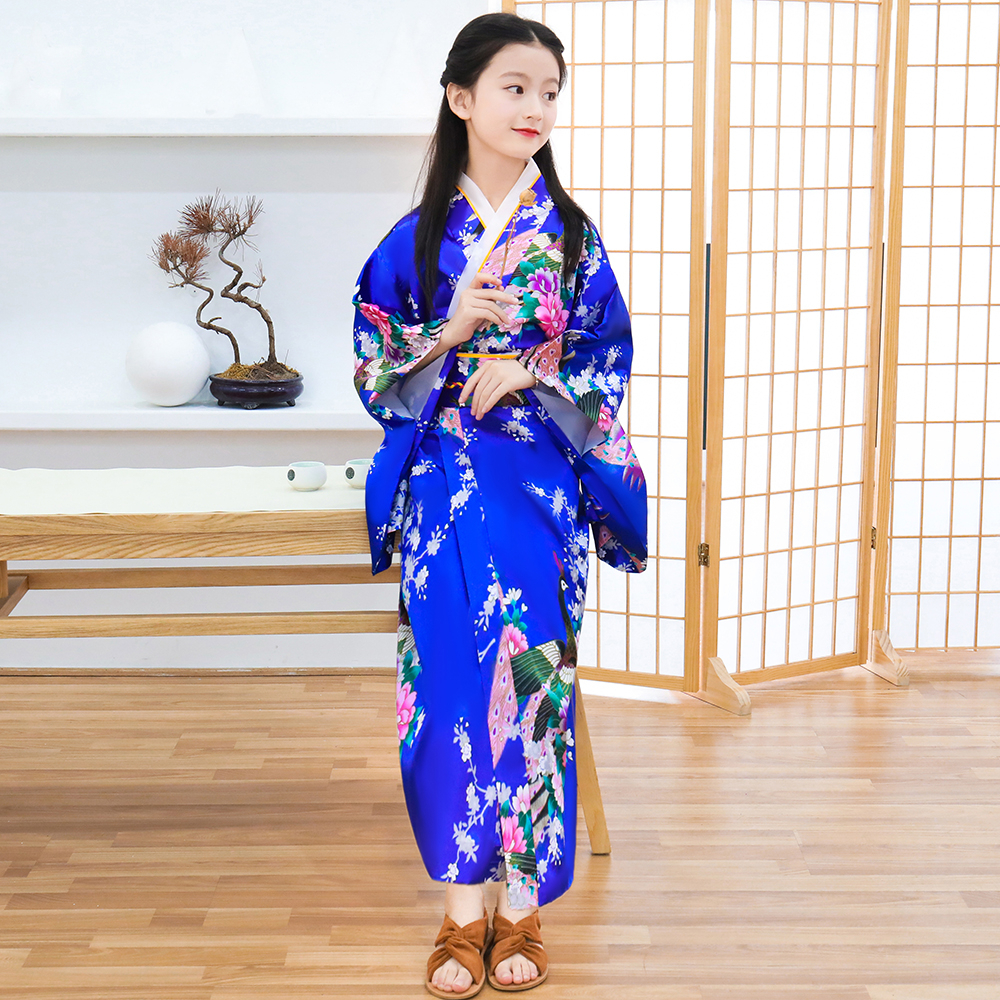 dans une pièces devant un paravent style japonais, une fillette porte un kimono bleu foncé avec un motif fleural