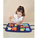 Petite fille posée sur une table à essayer d'ouvrir la fermeture Éclair sur la planche d'apprentissage avec différents objets comme un bouton, une pression , un cordon de serrage, un clip, une ceinture