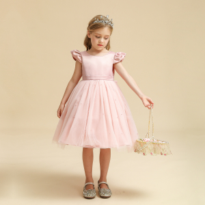 Une petite fille debout avce une robe rose en tulle, le fond est beige
