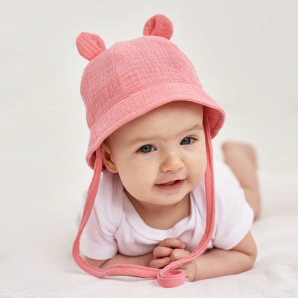 Bébé fille à plat ventre sur un tissu blanc nid d'abeille avec un body blanc et un chapeau de mousseline rose avec oreilles et cordelette.