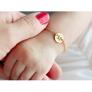 Bracelet avec gravure initiale pour bébé fille sur le poignet d'un bébé de couleur doré avec maillon à chaîne