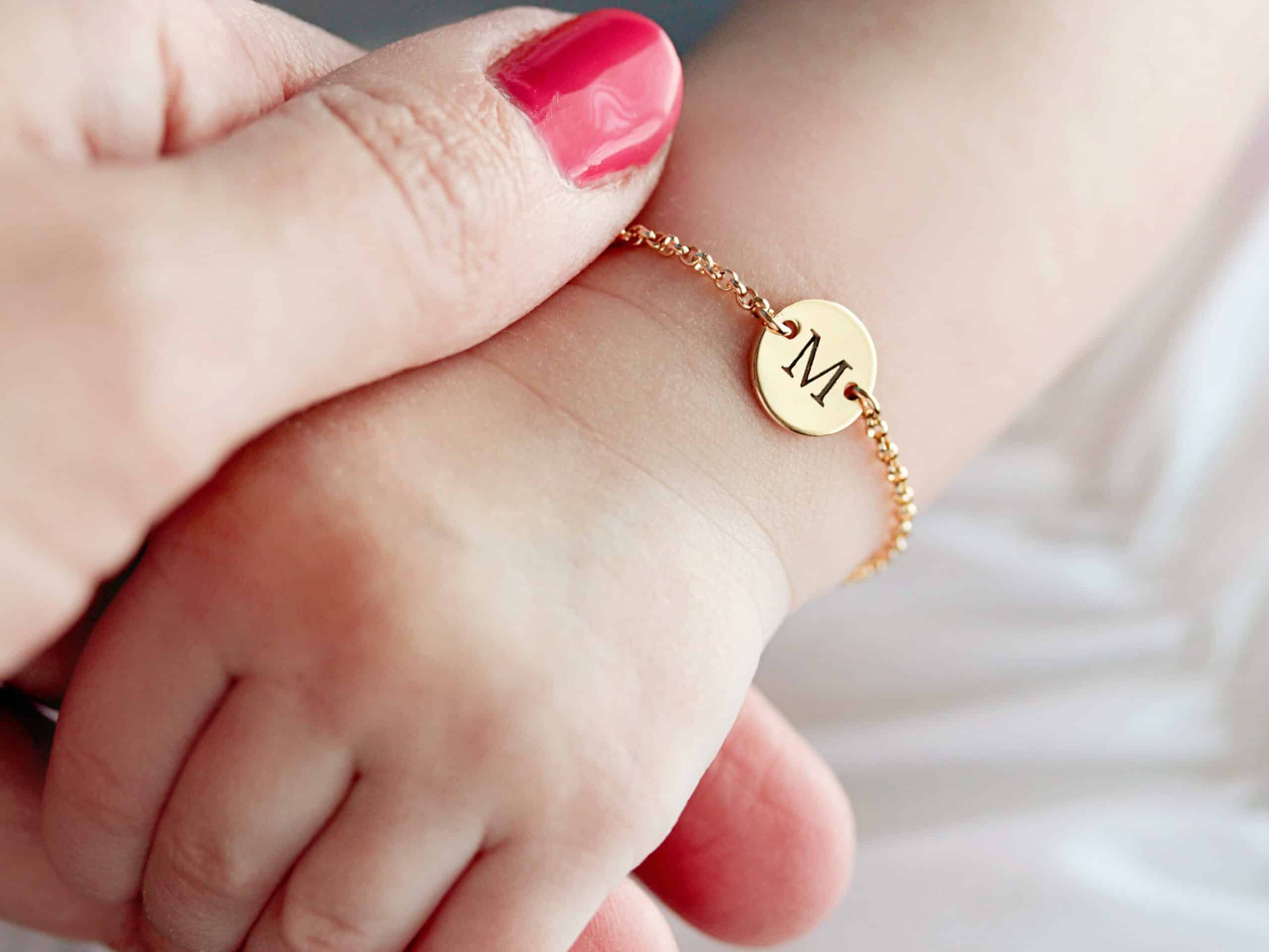 Bracelet avec gravure initiale pour bébé fille sur le poignet d'un bébé de couleur doré avec maillon à chaîne