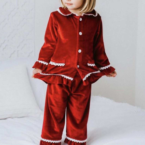 Petite fille blonde debout, portant un pyjama de Noël en velours rouge