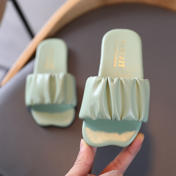 Claquettes vertes dont une est tenue dans une main et l'autre posée sur un élément gris