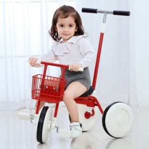 Petite fille brune assise sur un tricycle rouge dans une pièce près d'une fenêtre