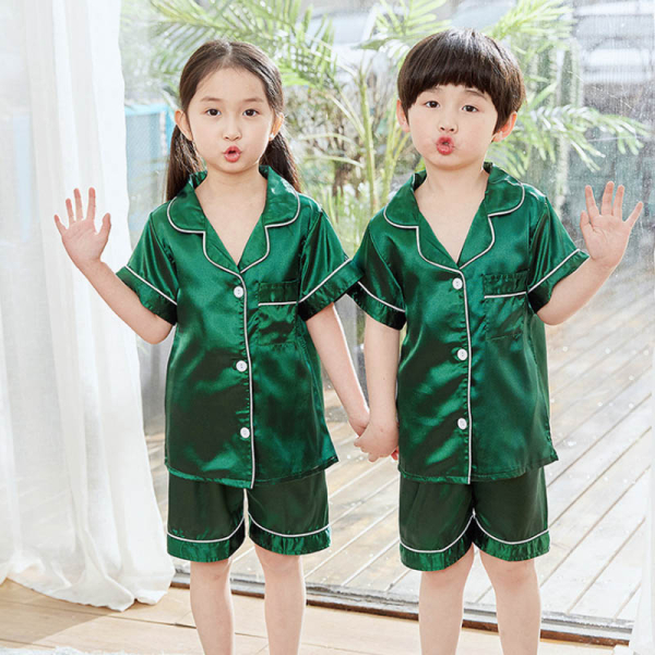 Jeune fille et jeune garçon debout, une main levée portant un pyjama satiné vert