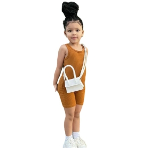 Petite fille brune avec des tresses et un chignon portant un combishort marron côtelé et un sac en bandoulière blanc
