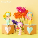 3 figurines Sonny Angel sur le thème floral, dont deux posées sur des boites en carton, avec un bouquet de fleurs en arrière-plan.