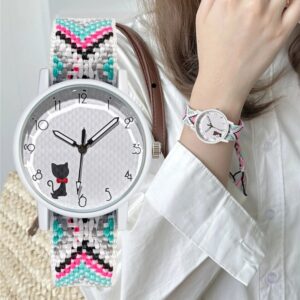 Une jeune fille porte une montre à quartz avec un bracelet tressé multicolore. Le cadran de la montre est orné d'un adorable chaton noir avec un nœud papillon rouge. Le bracelet est composé de fils tressés dans des teintes variées, incluant du rose, du turquoise, du noir, et du blanc, ajoutant une touche de gaieté et de style à la tenue.