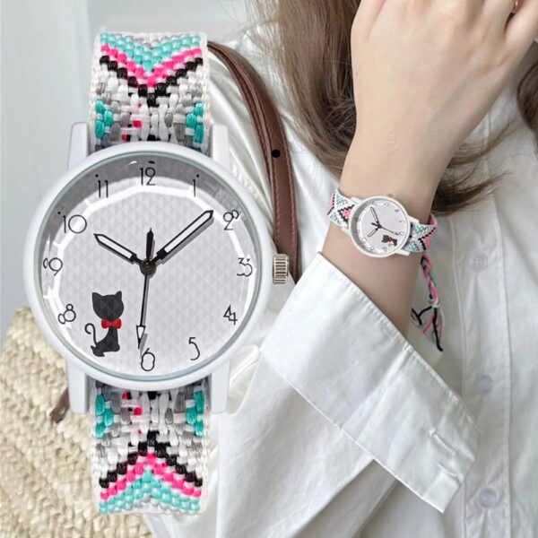 Une jeune fille porte une montre à quartz avec un bracelet tressé multicolore. Le cadran de la montre est orné d'un adorable chaton noir avec un nœud papillon rouge. Le bracelet est composé de fils tressés dans des teintes variées, incluant du rose, du turquoise, du noir, et du blanc, ajoutant une touche de gaieté et de style à la tenue.