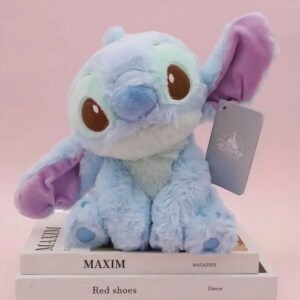 peluche stitch couleur bleu pastel, assis sur une pile de livre, sur fond rose.