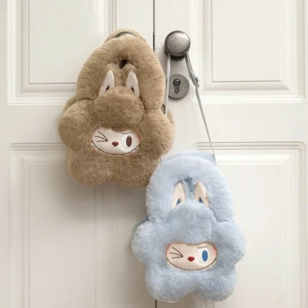 2 petits sacs à main moelleux en forme de fleur, avec visage Labubu clignant de l’œil et grandes oreilles de lapin. Un bleu doux et un marron clair accroché à une poignée de porte.