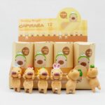 figurines capybara miniatures debout avec des bonnets différents, devant leurs boîtes, sur fond gris