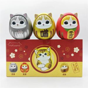 Set de 3 figurines mofusand en forme de chats daruma japonais colorés posés sur une boîte décorative rouge et jaune