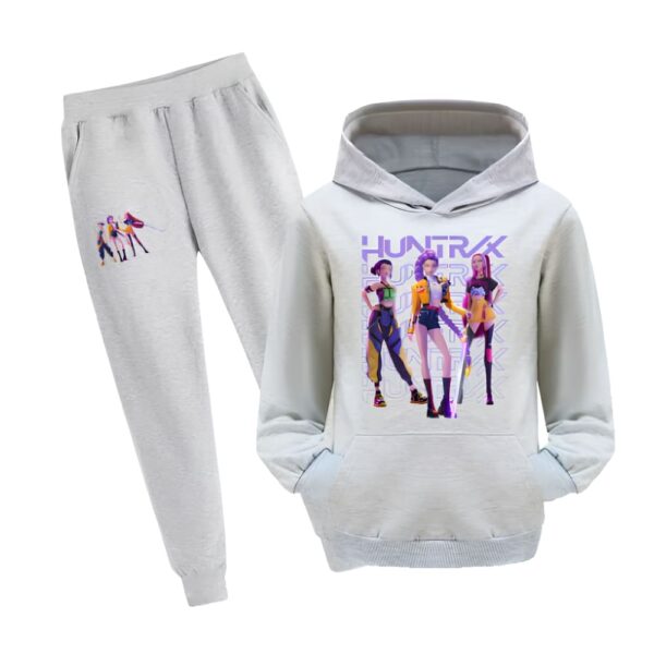 Jogging fille K-pop Demon Hunters avec sweat à capuche. L'ensemble est gris avec un motif sur la cuisse du pantalon et un gros motif avec les trois héroïnes du film sur le devant du sweat. Le sweat a une poche kangourou. Sur fond blanc.