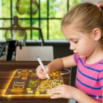 Petite fille dessinant sur un tableau lumineux LED réutilisable, avec des motifs colorés et des lettres visibles en lumière néon.