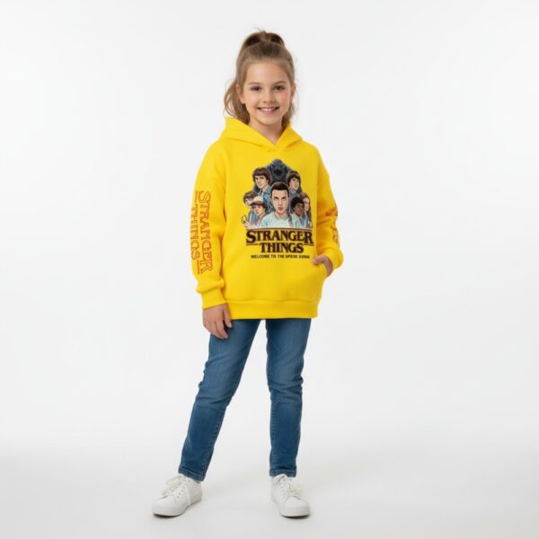 Petite fille portant un sweat Stranger Things jaune, sur fond gris