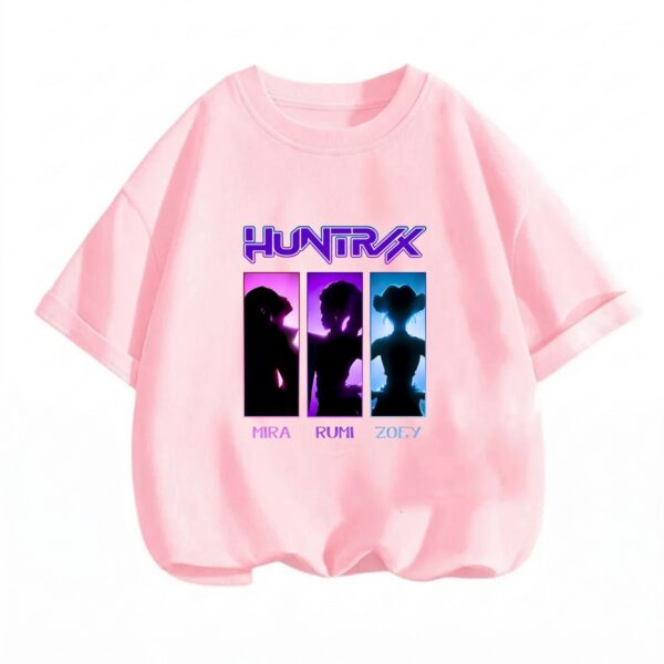Un T-shirt Demon Hunters trio fille rose, avec le logo et trois silhouettes de personnages, posé sur un fond blanc simple.
