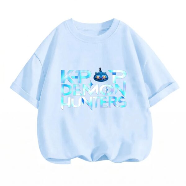 Un T-shirt fille K-pop Demon Hunters irisé bleu clair, avec un logo brillant au centre et un petit personnage sur le motif, présenté sur fond blanc.