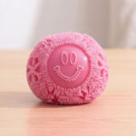 Une balle anti-stress squishy Needoh avec petits picots rose posée sur une table en bois.