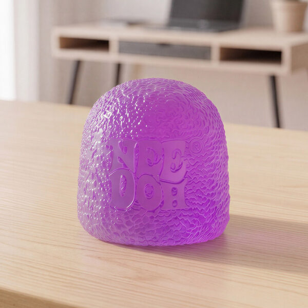 Un jouet squishy anti-stress Needoh gumdrop violet posé sur une table en bois, dans une pièce lumineuse avec un bureau et un ordinateur en arrière-plan.
